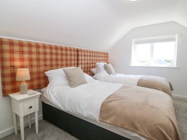 A bedroom with two single beds with plaid headboards and a lamp on a bedside table at Glanffraw in Aberffraw Ty Croes