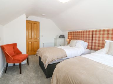 A bedroom with twin beds a red chair a wooden door and a white dresser at Glanffraw in Aberffraw Ty Croes