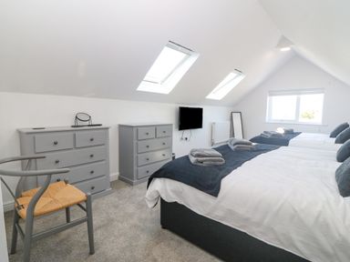 A bedroom with two beds two dressers a chair and skylight windows at Glanffraw in Aberffraw Ty Croes