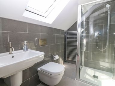 A bathroom with a wall-mounted sink and faucet a toilet a glass-enclosed shower and a towel rack with a skylight at Glanffraw in Aberffraw Ty Croes