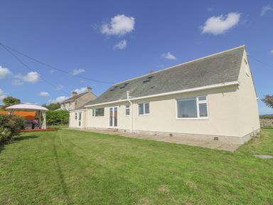 A single story house with a sloped roof and skylights surrounded by a lawn with a gazebo at Glanffraw in Aberffraw Ty Croes