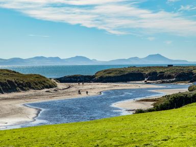 A coastal landscape with a river flowing into the sea and hills in the background at Glanffraw Aberffraw Ty Croes