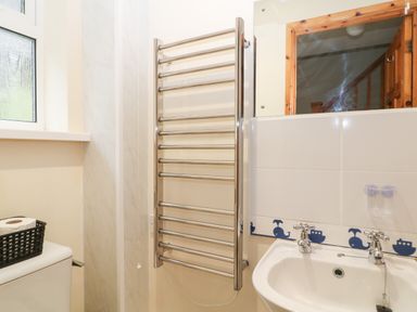 A bathroom with a toilet, wall-mounted towel radiator, sink, mirror, and window at Hembry Meadows in Honicombe Park near Gunnislake