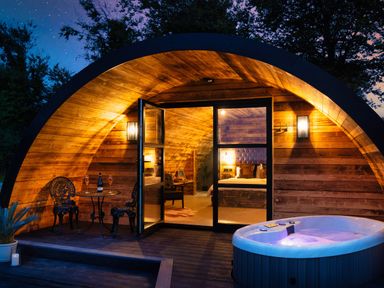 An arched wooden pod with a hot tub outside and a table with two chairs at The Piglet Pod in Llanarth