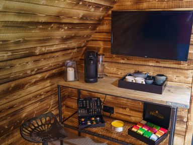 A wooden corner with a coffee machine cups tea box candle and television at The Piglet Pod in Llanarth