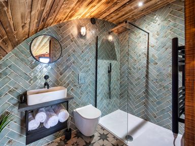 A bathroom with a walk-in shower a toilet a sink with towels underneath and a circular mirror at The Piglet Pod in Llanarth