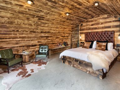 A bedroom with a large bed a wooden headboard two green chairs a wooden round table and a cowhide rug at The Piglet Pod in Llanarth