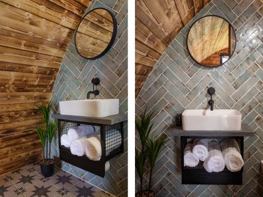 A bathroom sink with a round mirror above and rolled towels underneath next to a potted plant at The Piglet Pod in Llanarth