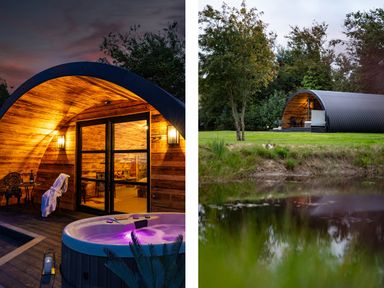 A curved wooden cabin with a hot tub in front near a pond surrounded by trees at The Piglet Pod in Llanarth