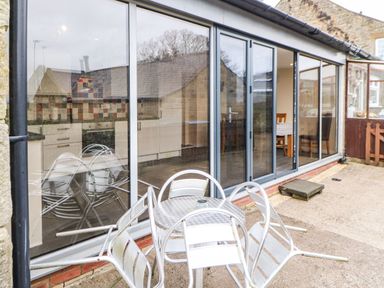 A patio with metal table and chairs outside a room with large glass sliding doors at Houghton North Farm Cottage in Heddon-on-the-Wall near Hexham