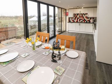 A dining table set with plates glasses and wine bottle next to a kitchen with white cabinets and black red white tiled backsplash at Houghton North Farm Cottage Heddon-on-the-Wall near Hexham