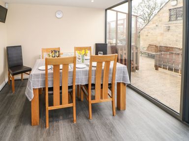 A dining room with a wooden table and chairs next to large glass sliding doors at Houghton North Farm Cottage in Heddon-on-the-Wall near Hexham