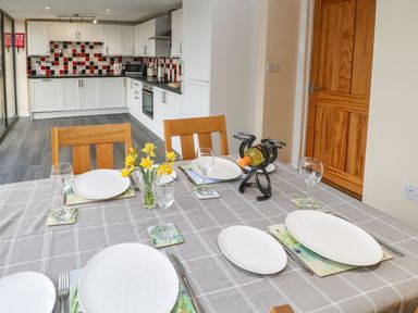 A dining table set with plates glasses cutlery and a vase of flowers next to a kitchen with white cabinets and a tiled backsplash at Houghton North Farm Cottage in Heddon-on-the-Wall near Hexham