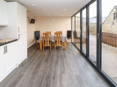 A dining area with a table covered by a checkered tablecloth and wooden and black chairs next to large glass sliding doors at Houghton North Farm Cottage in Heddon-on-the-Wall near Hexham