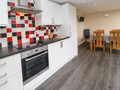 A kitchen with white cabinets red black and white tiled backsplash and a dining table with wooden chairs at Houghton North Farm Cottage in Heddon-on-the-Wall near Hexham