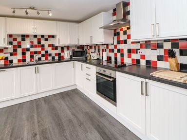 A kitchen with white cabinets black countertops and red black and white tiled backsplash at Houghton North Farm Cottage in Heddon-on-the-Wall near Hexham
