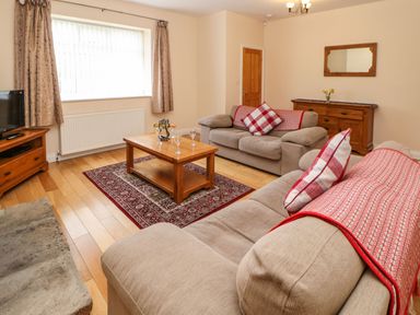 A living room with two sofas a wooden coffee table with wine glasses a wooden cabinet with a mirror and curtains at Houghton North Farm Cottage in Heddon-on-the-Wall near Hexham