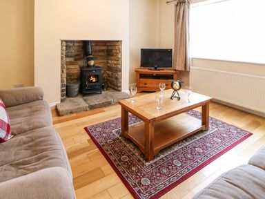 A living room with two sofas a wooden coffee table on a red patterned rug a fireplace with a wood stove and a television on a wooden stand at Houghton North Farm Cottage in Heddon-on-the-Wall near Hexham