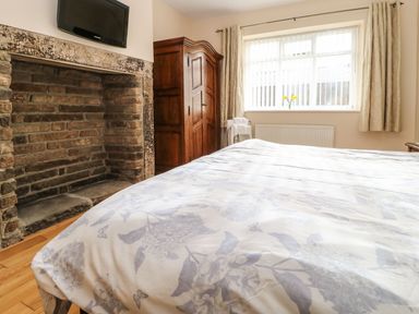A bedroom with a bed covered in floral bedding a brick fireplace a wooden wardrobe and a window with curtains at Houghton North Farm Cottage in Heddon-on-the-Wall near Hexham