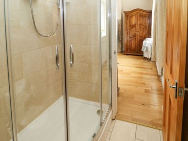 A shower enclosure with glass doors in a bathroom next to a wooden door and a wooden cabinet in a room with hardwood flooring at Houghton North Farm Cottage in Heddon-on-the-Wall near Hexham
