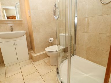 A bathroom with a white sink cabinet mirror toilet and curved glass shower enclosure at Houghton North Farm Cottage in Heddon-on-the-Wall near Hexham