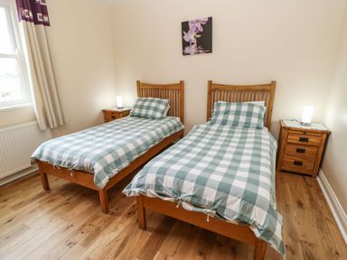 A bedroom with two single beds with checked bedding two wooden bedside tables with lamps and a window at Houghton North Farm Cottage in Heddon-on-the-Wall near Hexham