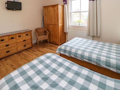 A bedroom with two beds with checked bedspreads wooden furniture and a window with flowers at Houghton North Farm Cottage in Heddon-on-the-Wall near Hexham