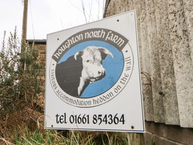 A sign for houghton north farm visitors accommodation heddon on the wall near a stone and metal structure at Houghton North Farm Cottage in Heddon-on-the-Wall near Hexham