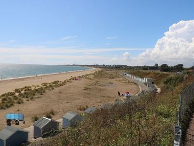 A sandy beach with beach huts and a path along the shore at Gull's Nest in Pakefield