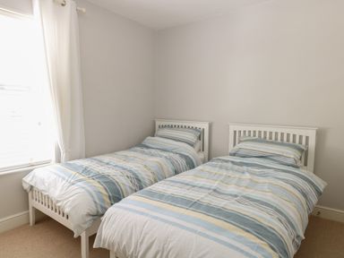 A bedroom with two single beds with striped bedding near a window with white curtains at Gull's Nest in Pakefield