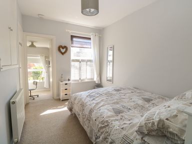 A bedroom with a bed a small white chest of drawers a wall mirror and a window with curtains at Gull's Nest in Pakefield
