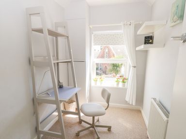 A small room with a white desk and chair near a window with potted plants on the sill at Gull's Nest in Pakefield
