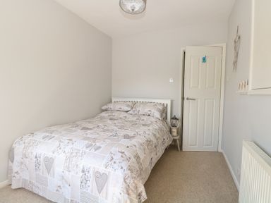 A bedroom with a bed covered by a patterned duvet a small bedside table with a lantern and a door at Gulls Nest in Pakefield