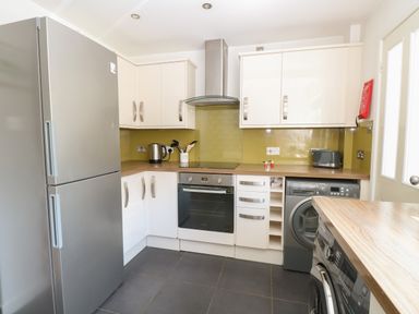 A kitchen with a refrigerator oven washing machine and cabinets at Gulls Nest in Pakefield