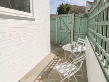 A small outdoor patio with a white table and two white chairs next to a white wall and a green wooden fence at Gulls Nest in Pakefield
