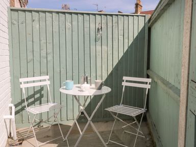 An outdoor patio with a small round white table and two white metal chairs at Gull's Nest in Pakefield