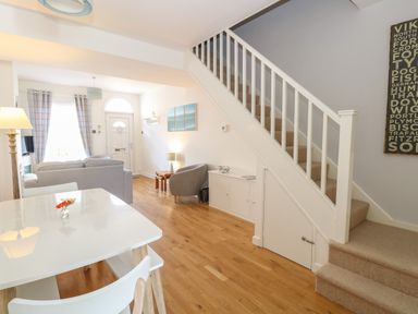 A living area with dining table chairs sofa armchair stairs and a front door at Gull's Nest in Pakefield