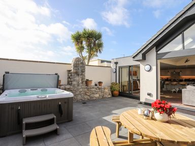 An outdoor patio with a hot tub wooden picnic table with flowers and a garden tap on a stone wall at The Herun in Rhosneigr
