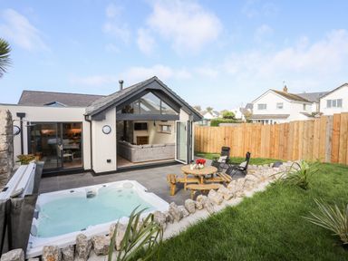 A backyard with a hot tub and wooden picnic table with chairs at The Herun in Rhosneigr