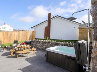 An outdoor patio area with a hot tub shower table with benches and chairs behind a stone wall at The Herun in Rhosneigr