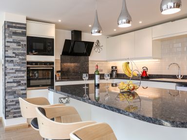 A kitchen with a black countertop island with wine glasses a wine bottle and fruit basket at The Herun in Rhosneigr
