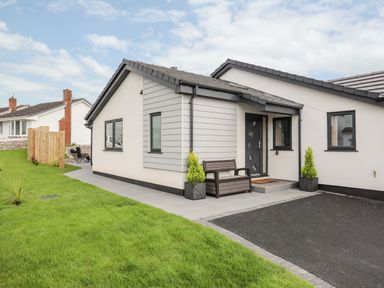 The exterior of a single story house with grass lawn a bench near the front door and two potted plants at The Herun in Rhosneigr
