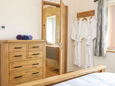 A bedroom with a wooden chest of drawers two rolled towels hanging white robes and an open door to a bathroom at The Herun in Rhosneigr