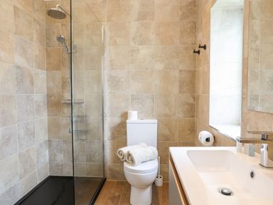 A bathroom with a glass shower enclosure a toilet with towels on top and a sink at The Herun in Rhosneigr