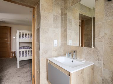 A bathroom sink with a mirror and toiletries near a bedroom with bunk beds at The Herun in Rhosneigr