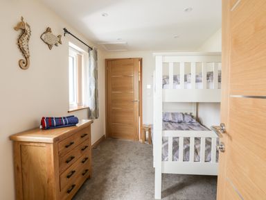 A bedroom with a white bunk bed a wooden dresser with towels and sea animal wall decorations at The Herun in Rhosneigr