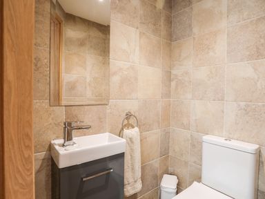 A bathroom with a sink cabinet a mirror a towel ring with a towel a trash bin and a toilet at The Herun in Rhosneigr