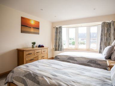 A bedroom with two single beds a wooden dresser a window with curtains and a sunset picture on the wall at The Herun in Rhosneigr