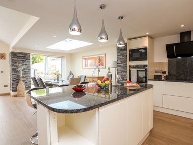 A kitchen with an island and dining area with chairs and table at The Herun in Rhosneigr