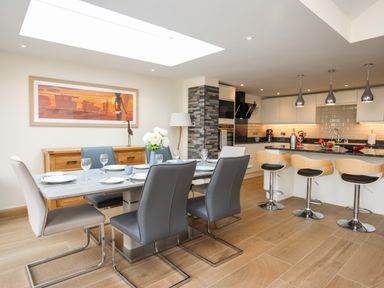 A kitchen and dining area with a dining table set with plates and glasses and bar stools at The Herun in Rhosneigr